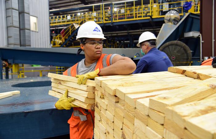 A woman holding lumber in a mill